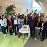 A group of colleagues standing around a cake which has a sustainability logo on it.