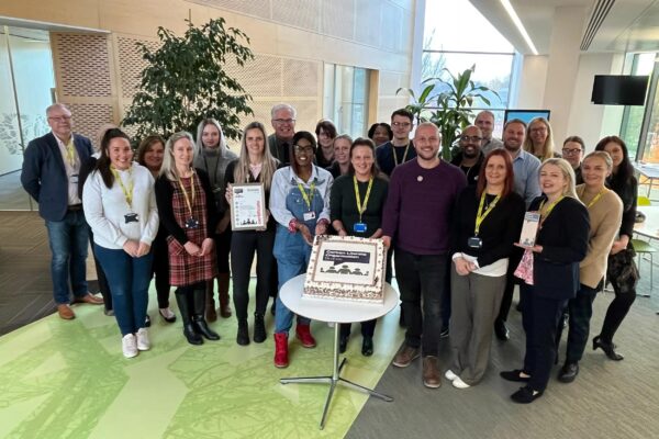 A group of colleagues standing around a cake which has a sustainability logo on it.