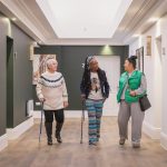 Three women walking down corridor in a residential building chatting to each other