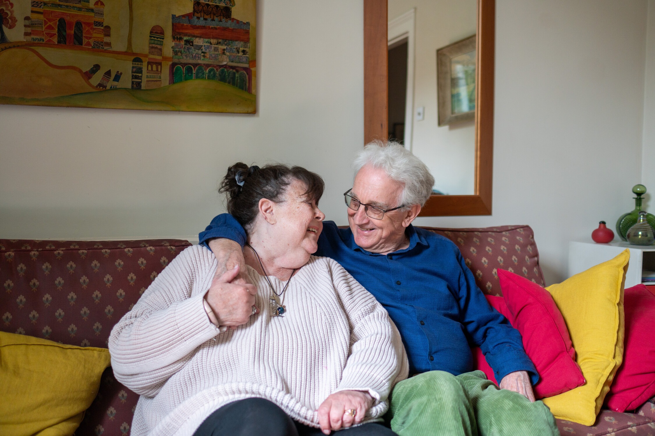 Two people sitting on sofa with their arms around each other
