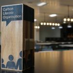 Wooden Carbon Literate Organisation award standing on a table in a modern, softly lit meeting room.