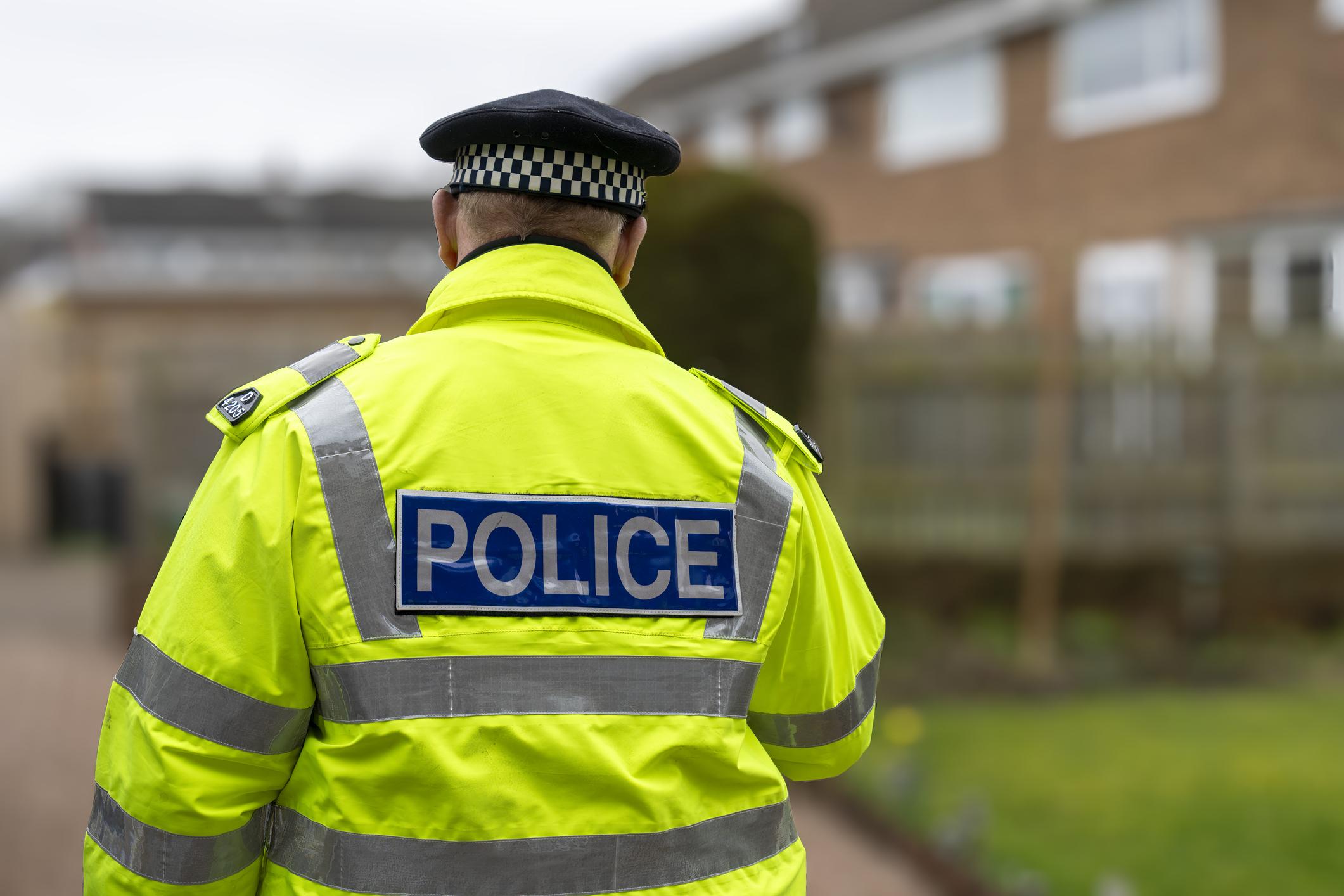 A policeman in high-vis uniform walking outside a home.