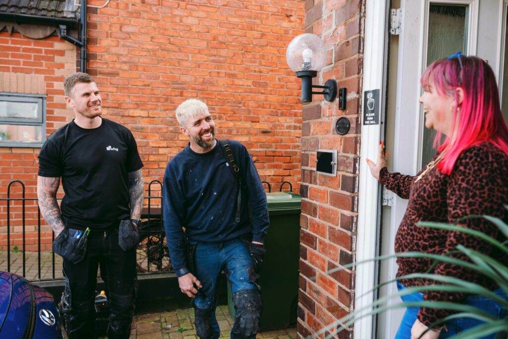 A customer greets two repairs tradespeople at the front door of her home.