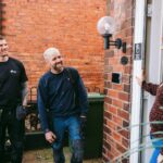 A customer greets two repairs tradespeople at the front door of her home.